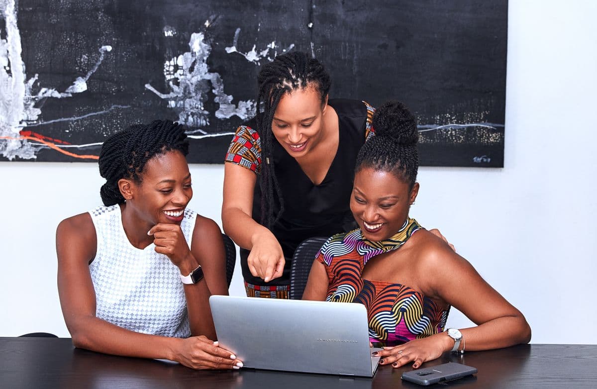 Three women gathered around a laptop, one pointing out something on the screen